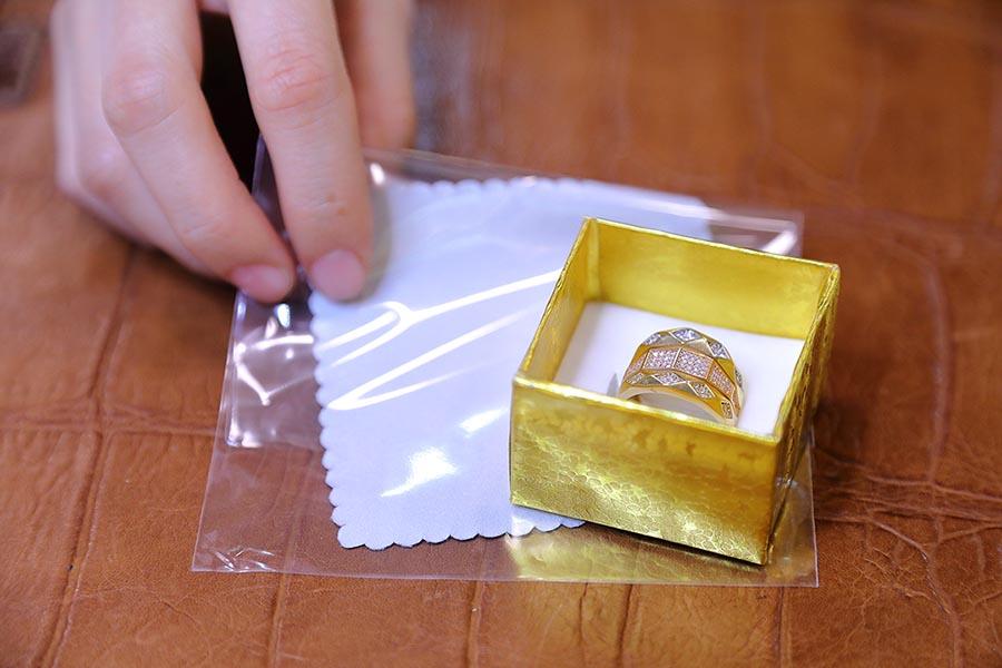 Az ékszerdobozban lévő arany gyűrű mellé szürke tisztítókendőt helyez egy női kéz