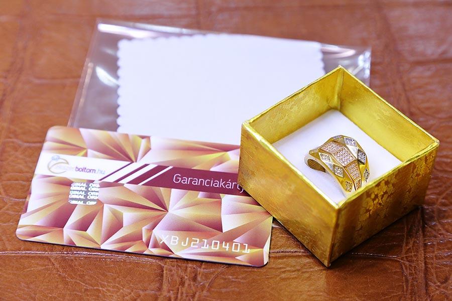 Barna bőr kínáló tálcán a tisztítókendő, garanciakártya és még nyitott díszdobozban az arany gyűrű